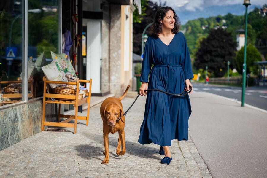 Frau im blauen Sommerkleid geht mit Hund an der Leine durch die Stadt spazieren
