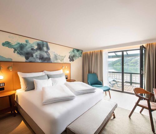 Großes Doppelbett im Hotelzimmer mit Balkon mit Blick auf den Millstätter See