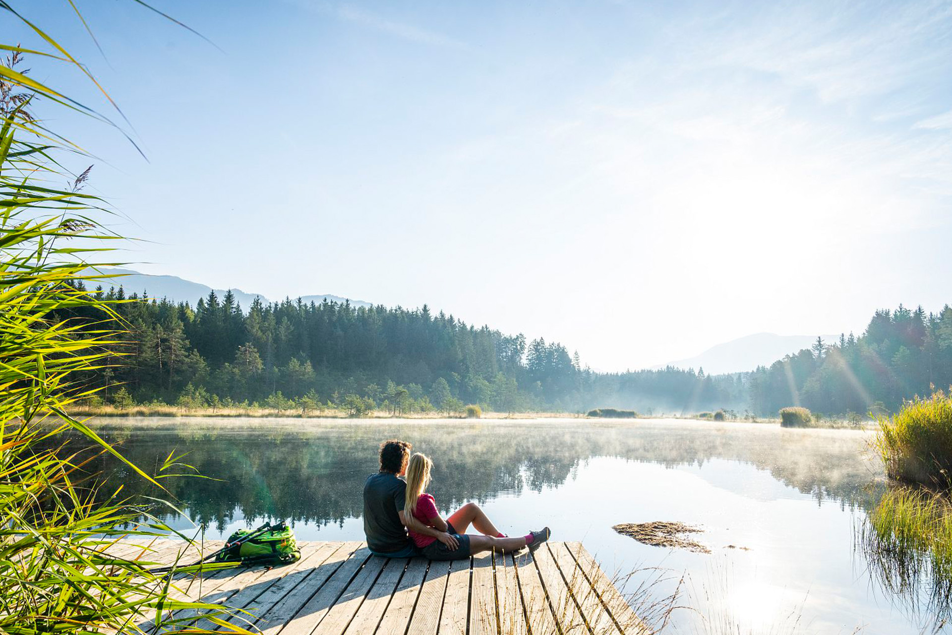 Sitzendes Paar am Steg blickt über den See