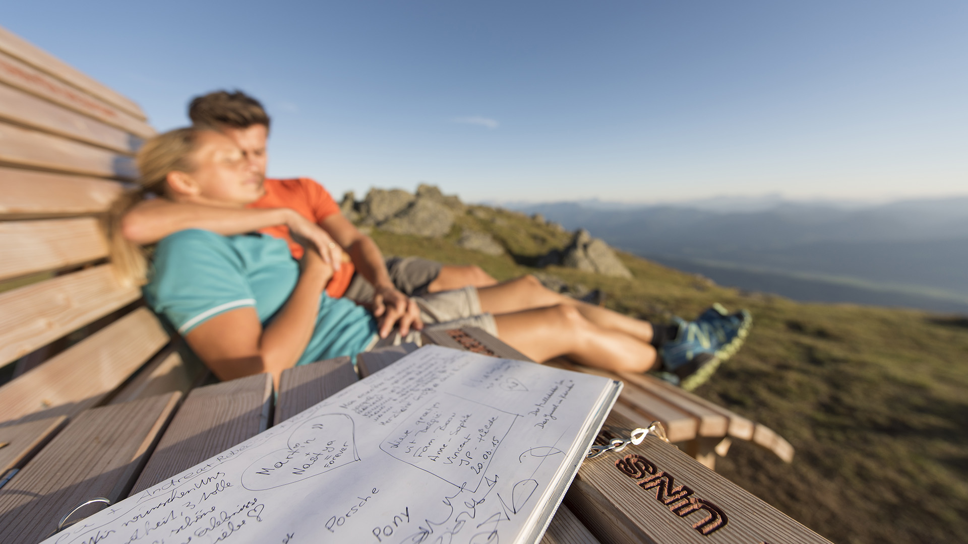 Paar sitzt umschlungen auf Bank in der Sonne